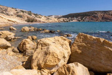 Agios Sostis sahilinin kayalık kıyılarında turkuaz sular altın kayalarla buluşur.