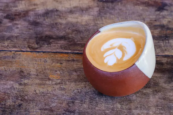 Düz beyaz bir kahvenin yakın plan bir resmi, eşsiz, toprak tonlu seramik bir fincanda, kırsal ahşap bir masaya yerleştirilmiş..