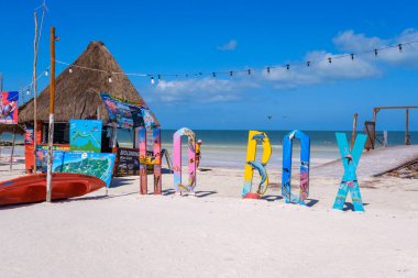 Holbox, Meksika - 9 Şubat 2025: Turkuaz deniz manzaralı bir kano ve gezi posterleriyle birlikte plajda renkli Holbox tabelası.
