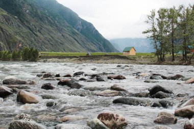 Altai Dağları 'ndaki Chulyshman nehrinin kıyısında bir ev. Sudaki taşlar, yeşil ağaçlar. Turist dinlenme merkezi. Yüksek kalite fotoğraf. yerli turizm