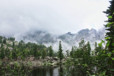 Ormandaki bir dağ gölü ve bulutlarla kaplı dağların mistik manzarası. Kötü havayla birlikte yaz günü. Ergaki doğa ulusal parkı, Khudozhnikov, Sibirya, Rusya