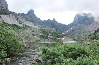 Gornykh Dukhov Gölü yüksek dağ tepeleriyle çevrilidir. Göl kıyısında görünen ağaçlar. Huzurlu ve huzurlu bir atmosfer, yalnızlık ve doğa ile uyum hissi yaratıyor. Ergaki Milli Parkı, Sibirya