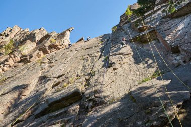 Ekipman içinde üç dağcı, mavi gökyüzü ve doğal arazi üzerinde bir halatla dik bir kayaya tırmanıyor. Yüksek kalite fotoğraf