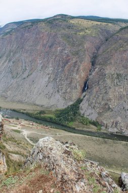 View from Katu-Yaryk pass to Chulyshman valley. High mountains with a waterfall, a river and a recreation center below. Summer season in Altai mountains. Vertical photo clipart