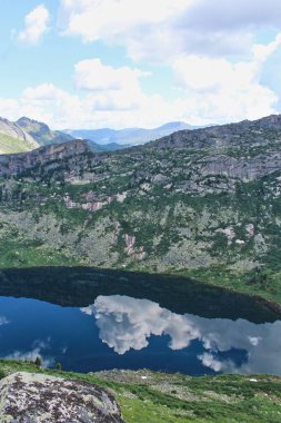 Dağ gölünün suyunda beyaz bulutların ve mavi gökyüzünün parlak yansıması. Ergaki doğa parkının manzarası. Krasnoyarsk bölgesi, Sibirya, Rusya. 