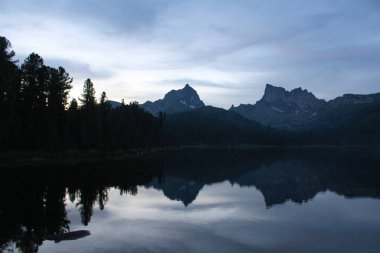 Svetloye gölünün suyuna iki kayalık dağ tepesi ve çam ağacı siluetleri yansıtılır. Ergaki doğa parkındaki doğa manzarası, Krasnoyarsk bölgesi, Sibirya, Rusya