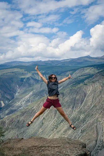 Travel is inspiring. A woman in a jump like stars against the backdrop of mountains. Summer trip Altai Republic, Siberia, Russia, Chulyshman valley, Katu-Yaryk pass.