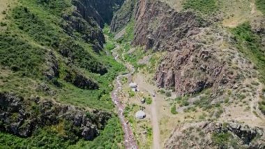 İnsansız hava aracı kayalık bir geçitte uçuyor. Dinlenen turistler, küçük nehir ve Kırgızistan 'ın etkileyici doğal manzarası olan yurt. Yüksek kalite 4k aeral görüntü