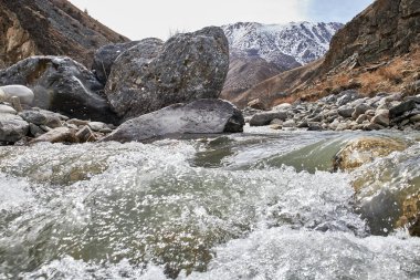 Hızlı akan dağ nehri. Su damlaları ve taştan bir dalga. Kar ilkbaharın başlarında dağları kapladı. Sezon dışı Doğal manzara yakın çekim