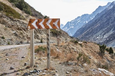 Dağlardan sola dönen tehlikeli bir yol işareti.