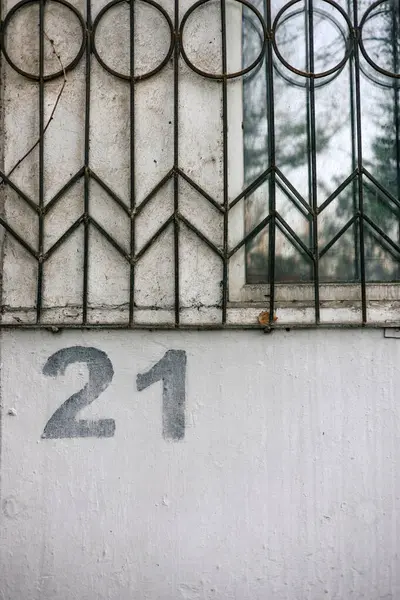 stock image The number twenty one is painted using a stencil on a gray wall below a window with bars. House numbering 21.