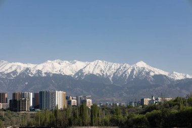 Dağların eteklerinde, tepeleri karla kaplı bir şehir. Tien Shan dağ sırasının arka planına karşı çok katlı binalar. Almaty, Kazakistan 'da bahar zamanı. Orta Asya kentsel