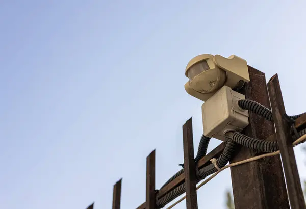 Street video surveillance and security system. Small Camera mounted on a metal fence against a blue sky.