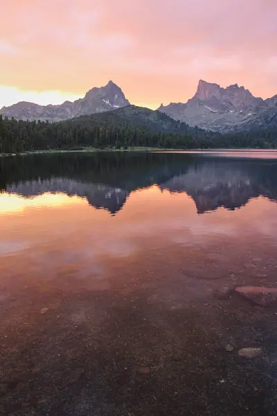Two mountains peaks are reflected in the crystal clear water of the lake at sunset. Selective focus