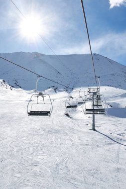 Kışlık tatil köyünde boş sandalyelerle kayak asansörü. Güneşli bir gün, mavi gökyüzü. Karlı Dağ yamacı. Ropeway İnşaat. Kış tatili aktivitesi. Chunkurchak, Bishkek, Kırgızistan