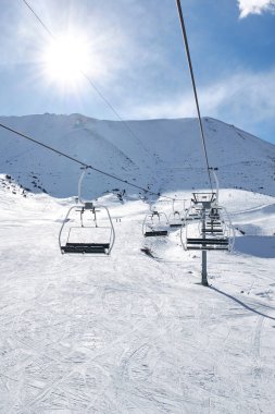 Ski lift with empty chairs at winter resort. Sunny day, blue sky. Snowy Mountain slope. Ropeway construction. Winter vacation activity. Chunkurchak, Bishkek, Kyrgyzstan clipart
