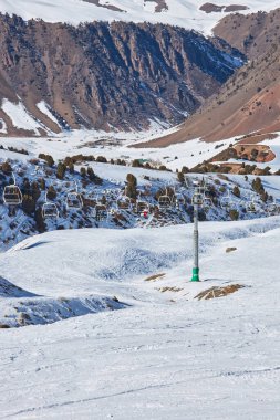 İnsanlar kayak pistinin tepesine çıkan teleferik sandalyelerinde oturuyorlar. Halat direği, inşaat. Kış tatili aktiviteleri, kayakçılar, snowboardcular, yaşam tarzı. Kırgızistan Doğası, Chunkurchak Tatil Köyü.. 