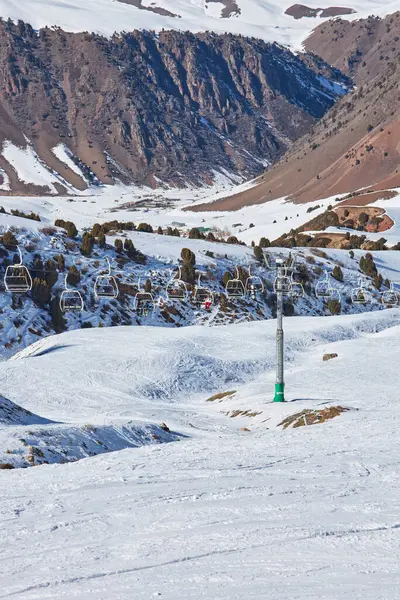 İnsanlar kayak pistinin tepesine çıkan teleferik sandalyelerinde oturuyorlar. Halat direği, inşaat. Kış tatili aktiviteleri, kayakçılar, snowboardcular, yaşam tarzı. Kırgızistan Doğası, Chunkurchak Tatil Köyü.. 