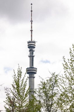 Büyük bir bina, ağaç dalları arasında televizyon kulesi manzarası. Televizyon yayın istasyonu ve radyo yayınları için antenlerin kurulduğu kule biçiminde anten direği yapısı