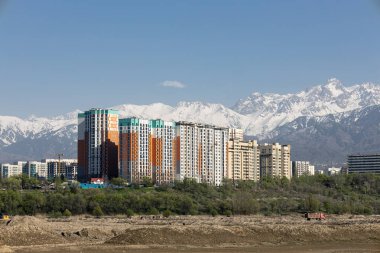 Şehir manzarası, en iyi dağ manzaralı konut kompleksi. Apartman binaları yüksek karlı dağların arka planına karşı. Almaty, Kazakistan. Uzayı kopyala, mavi gökyüzü. Şehrin ve doğanın birliği