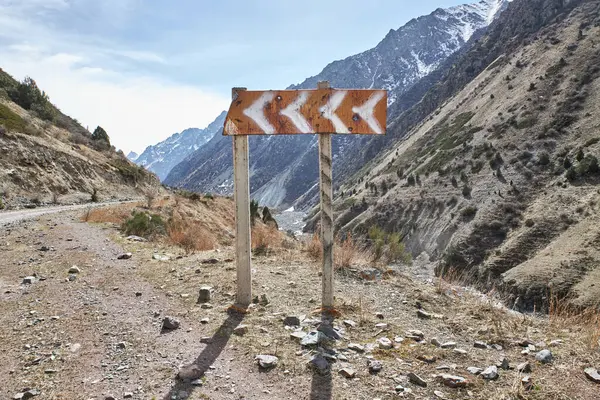 Old traffic sign on the side of the road indicating a left turn in the mountains on the background of a natural landscape. Dangerous section of road in the mountains, on the way to the pass