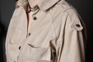 Göğsünde cebi, üçgen düğmeleri, tasması ve omuz kemeri olan kadın bej gömleği. Yan görüş. Bir kadında kalın pamuklu ceket. Kıyafet dikmek, moda alışverişi.