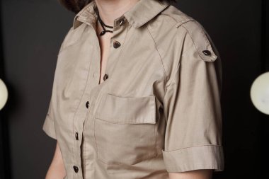 Kadın düz bej gömlek göğüs, üçgen düğmeler, yaka ve omuz kayışları, kolları kıvrımlı. Bir kadında kalın pamuklu ceket. Kıyafet dikmek, moda alışverişi.