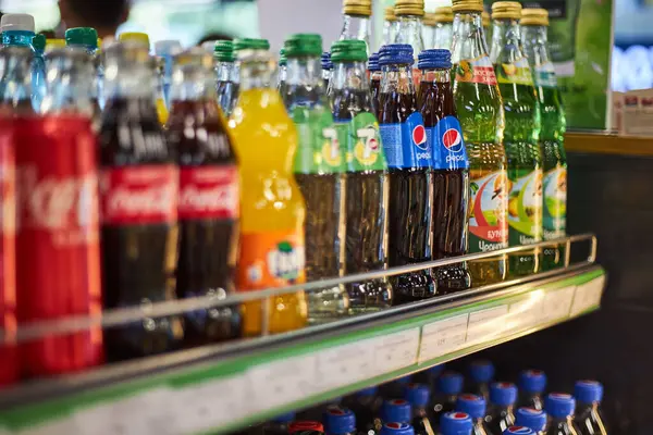 Markette raflar, farklı marka gazozlar. Coca Cola, Fanta, 7 numara Pepsi. Alüminyum kutular, çeşitli boyutlarda cam şişeler. Meşrubat başyazısı, popüler karbonatlı içecekler. Bishkek, Kırgızistan - 26 Mayıs 2023