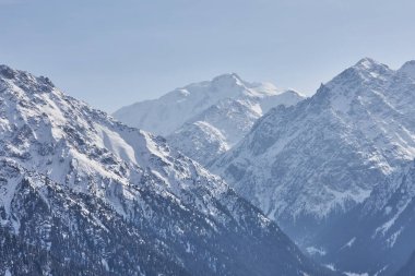 Dağ sırası, karlı tepeler, orman ve dağlık arazi arasındaki sınır. Doğal manzara arka planı. Karakol vadisi manzarası. Kırgızistan dağlarında kış. Orta Asya, Kirgiziya, dinlenme alanı.