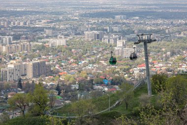 Kazakistan 'daki Kok Tobe tepesine hava desteği. Bahar zamanı Almaty City 'nin arka planına karşı iki kabinli kablolu araba. Turistik bir yer, şehir simgesi. Halat destek sütunu