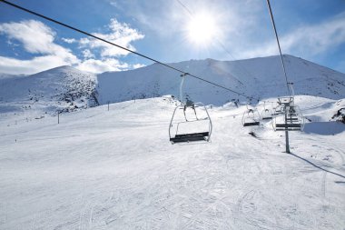 Ski lift pole with empty chairs at winter resort. Sunny day, blue sky. Mountain slope. Ropeway construction. Winter vacation activity. Chunkurchak, Bishkek, Kyrgyzstan clipart