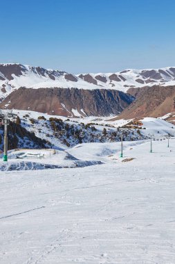 Halat direği, inşaat. Kış tatili aktivitesi, yaşam tarzı sporu ve eğlence. Kayakçılar ve snowboardcular dağ yamacının zirvesine çıkan bir teleferikle yukarı çıkıyorlar. Tatil Köyü Chunkurchak, Kırgızistan