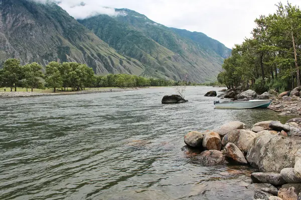 Dağ nehrinin kıyısındaki ahşap bir rıhtıma demirlemiş küçük bir tekne, yaz manzarası, Chulyshman Vadisi, Altai Cumhuriyeti, Sibirya, Rusya 'dan geçiyor. Yüksek kalite fotoğraf