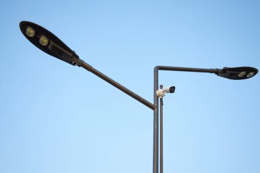 Tek direkten iki çağdaş sokak lambası, birden fazla LED ampulle donatılmış. Güvenlik kamerası, şehir parkındaki güvenlik. kentsel altyapı, ışıklandırma ve izleme teknolojisini birleştirir