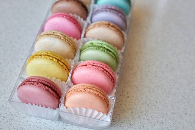 Beyaz kağıt kalıplı parlak Fransız makarnaları, mutfak tezgahında şeffaf plastik ambalaj kutusu, çeşitli tatlarda renkli kekler. Kurabiye iştah açıcı. Metin için alanı kopyala, seçici odak