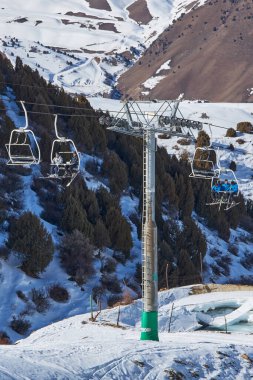 İnsanlar kayak pistinin tepesine çıkan teleferik sandalyelerinde oturuyorlar. Halat direği, inşaat. Kış tatili aktiviteleri, kayakçılar, snowboardcular, yaşam tarzı. Resort Chunkurchak, Kırgızistan - 21 Şubat 2023. 