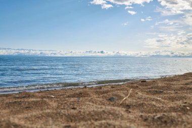 Issyk-Kul Gölü, kumlu plaj, büyük göl kıyısı, Kırgızistan 'da yaz tatili. Göletin mavi renkli suyu, küçük dalga. Kirgiziya 'nın gideceği yer. Bulutlardaki dağlar