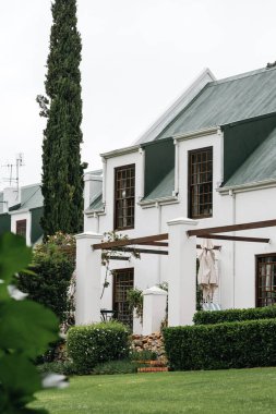 Porsiyon konut klasik mimari tarzı. Yeşil kiremit çatılı beyaz cephe. Ahşap çerçeveli büyük pencereler, dekoratif elementler sütunları korozyona uğratıyor. Yeşillik binayı çevreledi