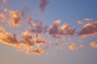 Mavi gökyüzünde günbatımı renkleriyle boyanmış küçük bulutlar. Açık romantik arkaplan, doğal eğimli altın rengi