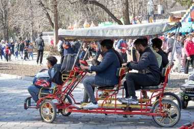 Parkta kiralık dörtlü bisiklete binen adamlar. Beş kişilik çift kişilik bisiklet. Bishkek, Kırgızistan - 21 MAR 2023