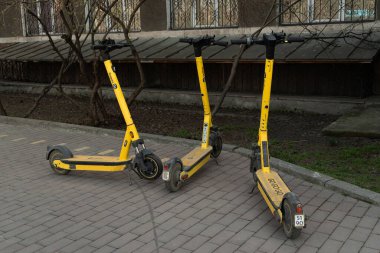 Yandex marka üç sarı elektrikli scooter kaldırım taşlarının üzerinde duruyor. Bishkek, Kırgızistan - 21 MAR 2025