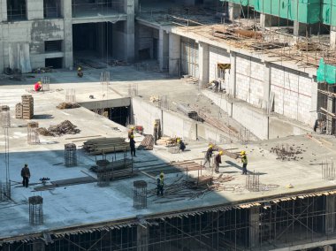 İşçiler, kancaya takılmış bir vinç tarafından indirilen bir demiri alıyorlar. Apartman inşaatı.