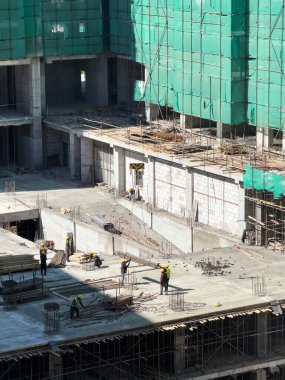 İşçiler, kancaya takılmış bir vinç tarafından indirilen bir demiri alıyorlar. Apartman inşaatı.