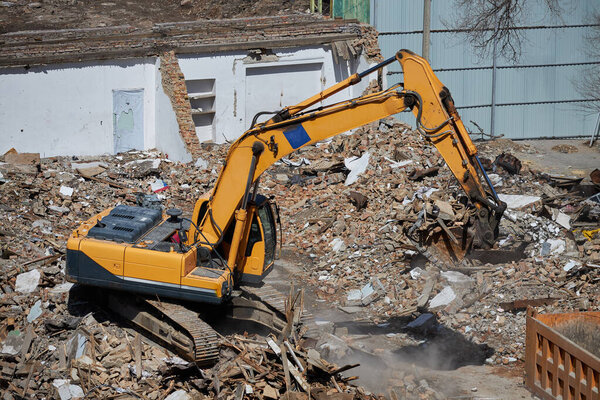 Excavator stands on a pile of construction waste with full bucket.