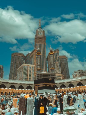 MECCA, SAUDI ARABIA-JULY 6, 2023: Unidentified Muslim pilgrims circumambulate the Kaabah in Makkah, Saudi Arabia with Abraj Al Bait (Royal Clock Tower Makkah) or Zamzam tower in the backgroud clipart