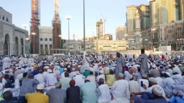 MECCA, SAUDI ARABIA KINGDOM (KSA) - 13 Haziran 2023: Müslüman hacılar, arka planda Suudi Arabistan 'ın Makkah kentindeki Abraj Al Yem binası ile Kutsal Cami' nin dışında akşam namazı için bekliyorlar.
