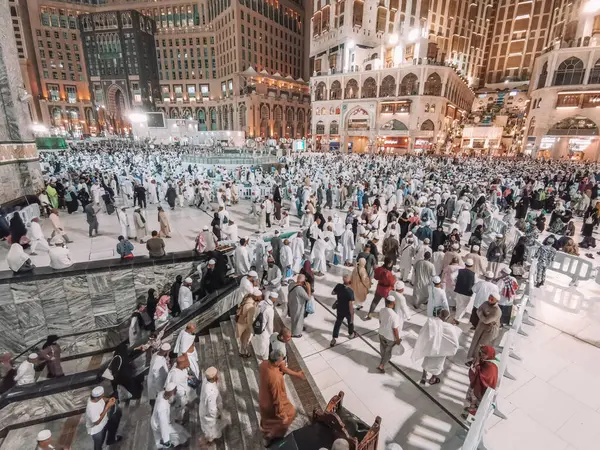 stock image MECCA, KINGDOM OF SAUDI ARABIA (KSA) - JUNE 5, 2023:Muslim hajj pilgrims exit Al Haram mosque after evening prayers with Abraj Al Bait Zamzam tower (L) and Hilton Hotel Makkah (R) in the background.