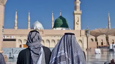 Arka planda, kimliği belirsiz, keffiyeh giyen iki Müslüman adamın Medine, Suudi Arabistan 'daki Nabawi Camii' nin yerleşkesindeki yeşil kubbeye baktığı görülüyor..