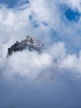 Kayalık bir dağın zirvesi bulutların arasından aydınlanan güneş ışığıyla aydınlanır, Dolomitler, İtalya