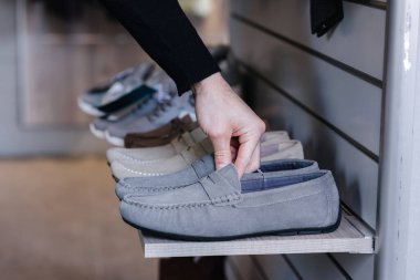 İnsan eli elbise mağazasındaki raftan gri mokasenleri alıyor..